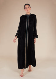 Woman wearing a black abaya with gold trim on a beige background