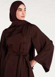 This mid-weight abaya boasts a subtle shine and features a flared silhouette, an oriental-style neckline, self fabric buttons and includes an optional belt. Dark brown colour. 