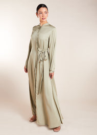 Discover the elegant and versatile Side Tie Abaya in an exquisite soft sage colour, crafted from a luxurious cotton satin blend that provides a subtle sheen. This abaya features a unique attached side belt that adds shape and dimension to the garment. 