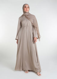 This waist pleat abaya in beige boasts a flattering fit with light pleating on the waist and bodice. Perfect for summer, the flared bell sleeves add a breezy touch, while the discreet button opening on the front of the bodice adds a thoughtful detail.